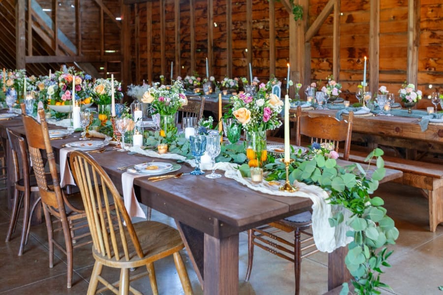 Reception tables with flowers, candles, and greenery inside a cozy barn wedding venue.