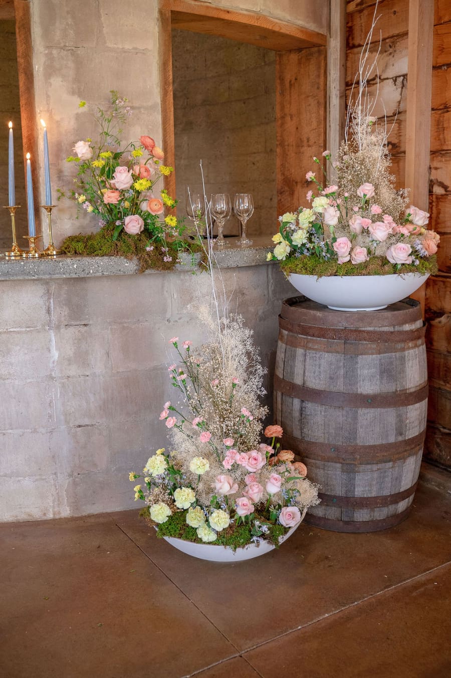 Floral arrangements with candles and soft pastel blooms decorating a rustic barn wedding bar area.