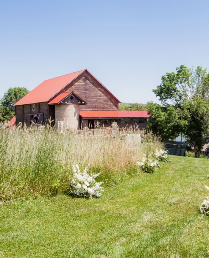 The Barn on Hubbard with its red roof and garden ceremony aisle surrounded by wild grass, an ideal setting for a wedding weekend in the Catskills.