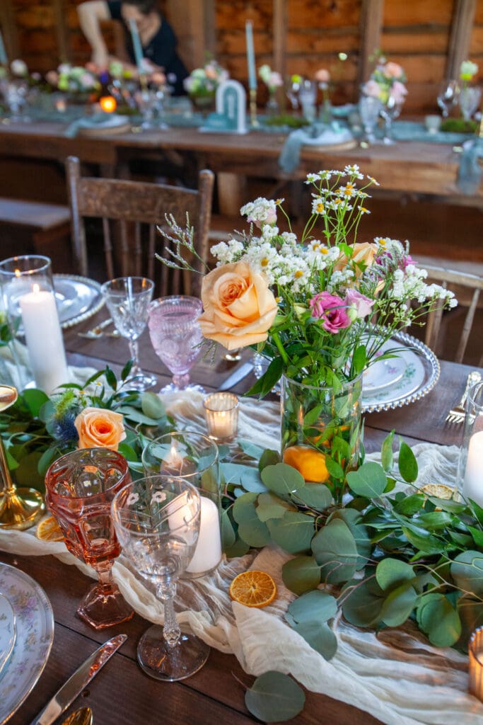A rustic reception table with floral centerpieces, candles, and vintage glassware inside The Barn on Hubbard during a wedding weekend in the Catskills.