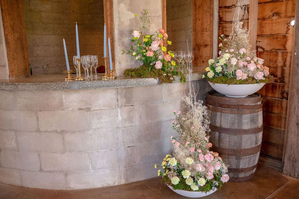 A charming indoor bar styled with romantic floral arrangements and candles inside The Barn on Hubbard for a wedding weekend in the Catskills.