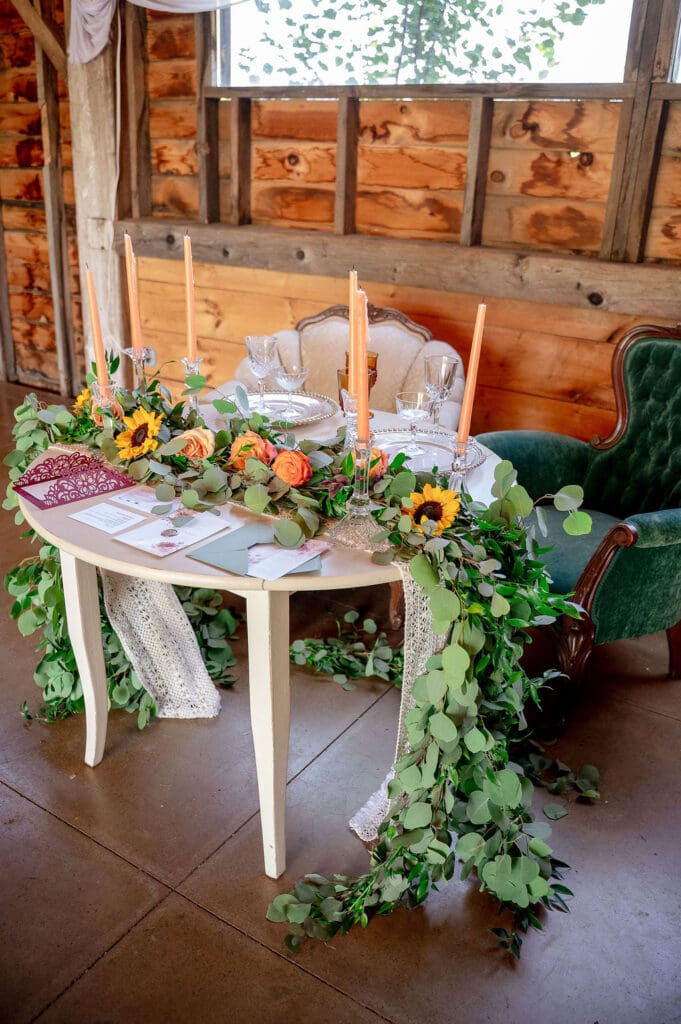 A sweetheart table decorated with sunflowers, roses, and candles inside The Barn on Hubbard during a wedding weekend in the Catskills.