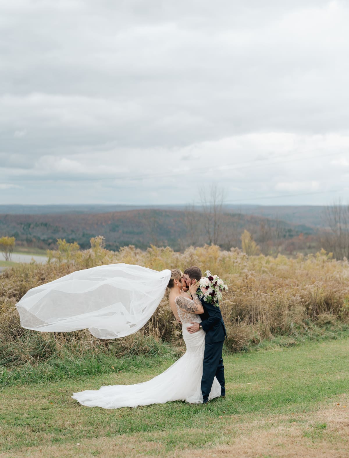 Couple kissing on a hillside with sweeping Hudson Valley views, capturing a romantic moment made possible by scenic, affordable wedding venues in the countryside.