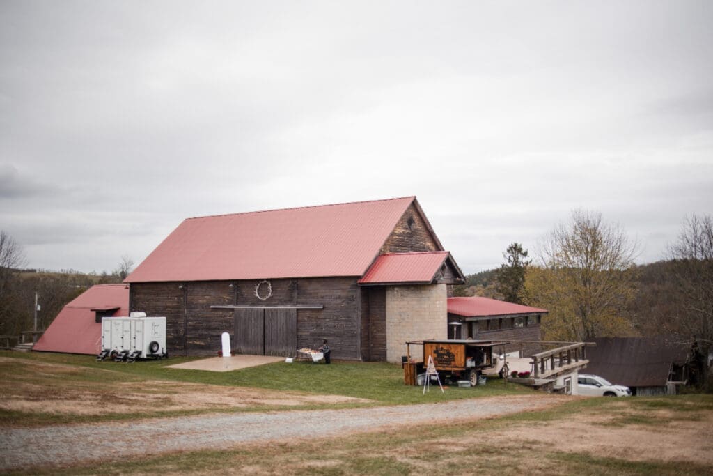 Wide exterior view of a restored barn venue with open grounds and vendor setup, highlighting the flexibility and space often included with affordable wedding venues.