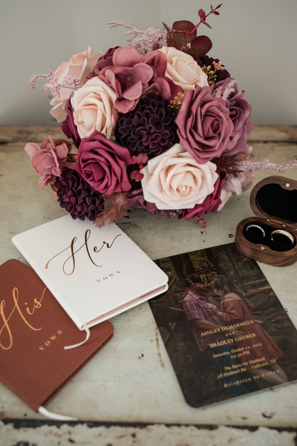 His and her vow books, a rich burgundy and blush bouquet, wedding rings in a walnut box, and a custom invitation for a Barn on Hubbard wedding. Every detail on your wedding vendor list telling one story.
