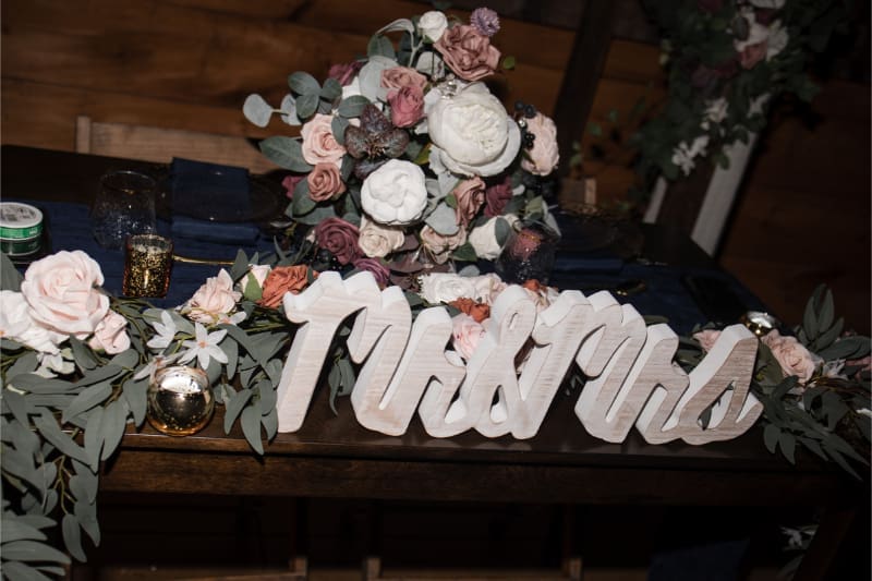 Wedding sweetheart table decorated with soft florals, greenery, candles, and personalized wedding signage.