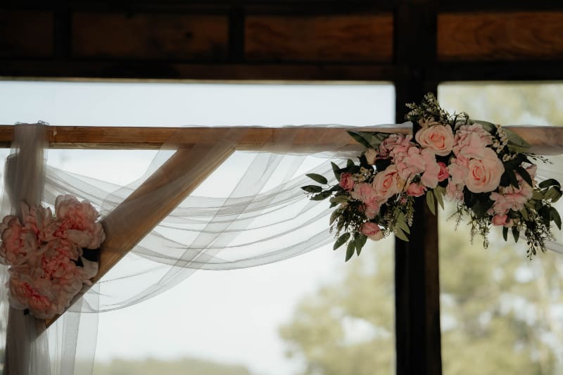 Barn wedding decor ideas featuring a wooden ceremony structure with soft draping, pink roses, and greenery.