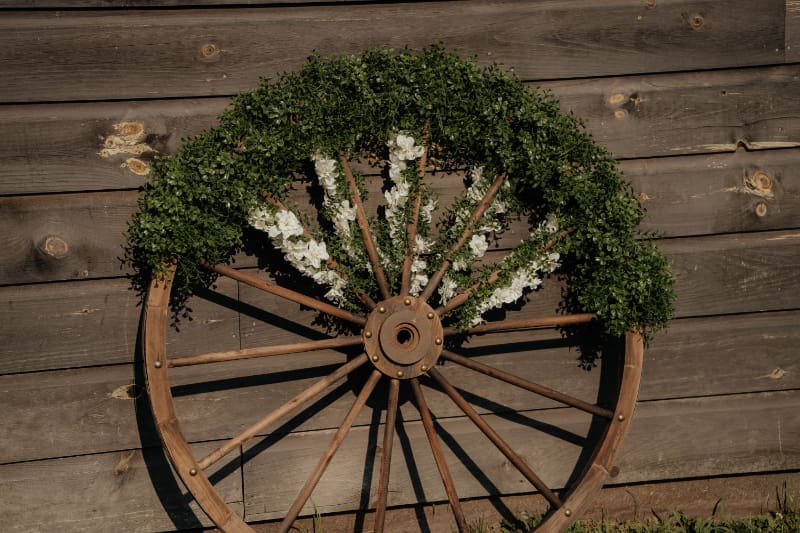 Barn wedding decor ideas featuring a vintage wagon wheel decorated with greenery and white flowers.