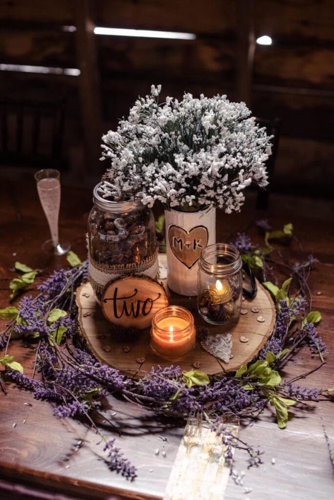 Rustic table centerpiece with lavender, baby’s breath, mason jar candles, wood slice, and table number two.