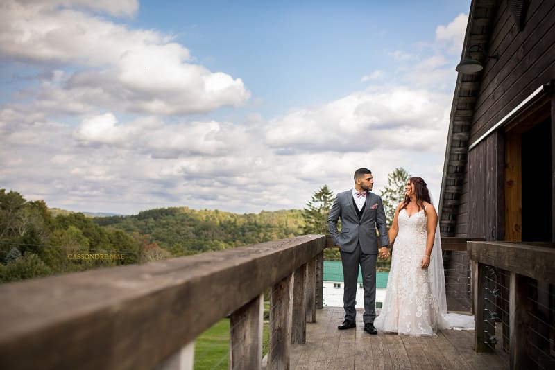 Bride and groom hold hands on the wooden deck at The Barn on Hubbard with rolling Catskills hills in the distance, highlighting the venue’s outdoor scenery when researching questions to ask your wedding venue.