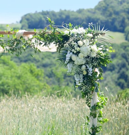 Outdoor wedding arch covered in white flowers and lush greenery, overlooking rolling countryside for a romantic fall foliage wedding ceremony.